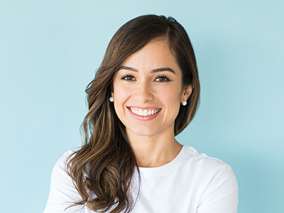 A smiling woman with long hair, wearing a white top, against a blue background.