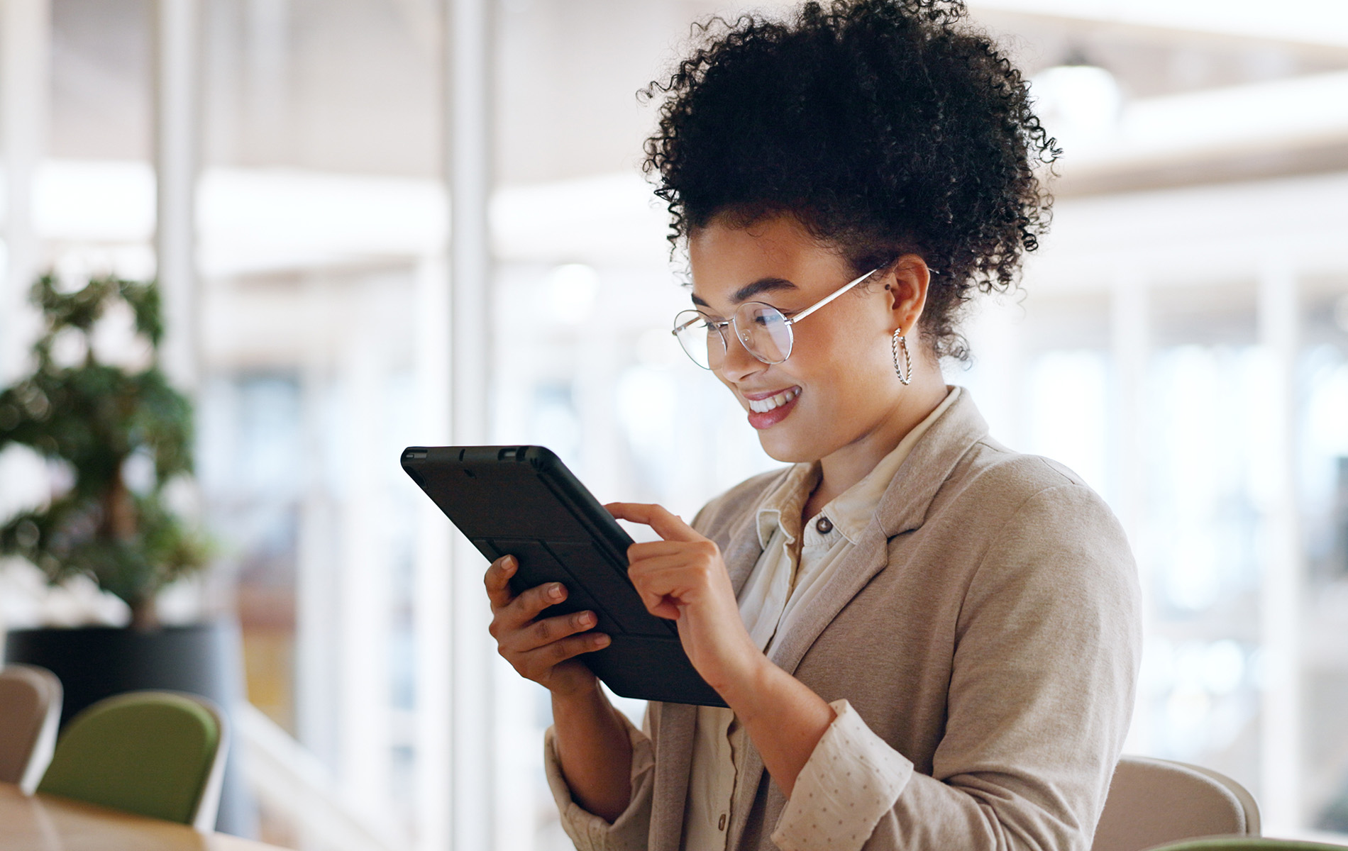 A person holding a tablet, smiling and looking at the screen while seated in an office environment.