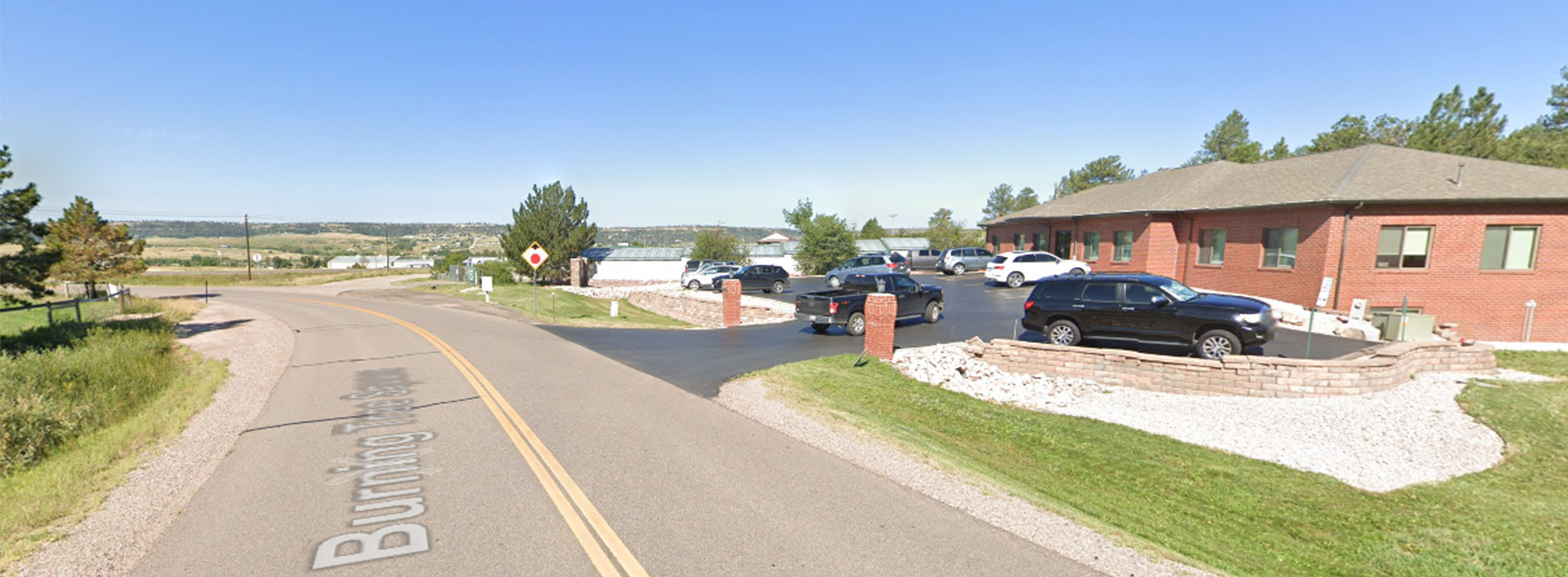 The image shows a split-screen photograph of a street scene, with the left side depicting a clear day under blue skies and the right side displaying an overcast sky. Both sides feature a residential area with houses, cars parked on the driveway, and a paved road leading to a cul-de-sac. The left image is taken during the daytime while the right one appears to be taken in the evening or at dusk.