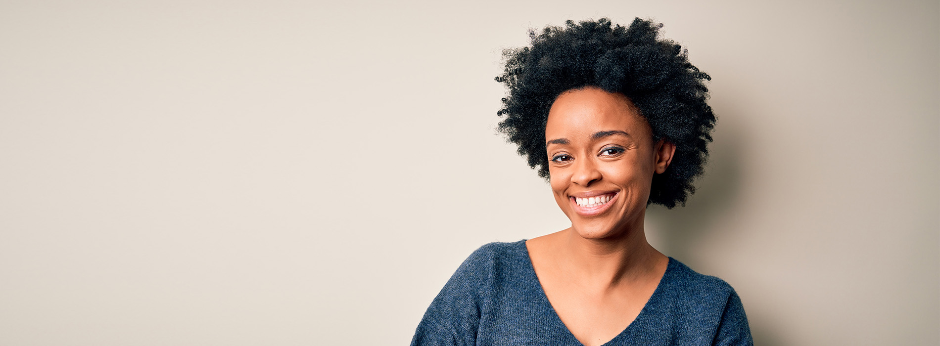 The image is a photograph of a woman with light skin, smiling at the camera. She appears to be in her late twenties or early thirties and has long hair. Her eyes are looking directly at the camera, and she is holding up her index finger near her mouth as if she s making a point or emphasizing something. The background is plain and light-colored, which suggests that this could be a stock photo used for various purposes such as advertising, personal branding, or lifestyle content.