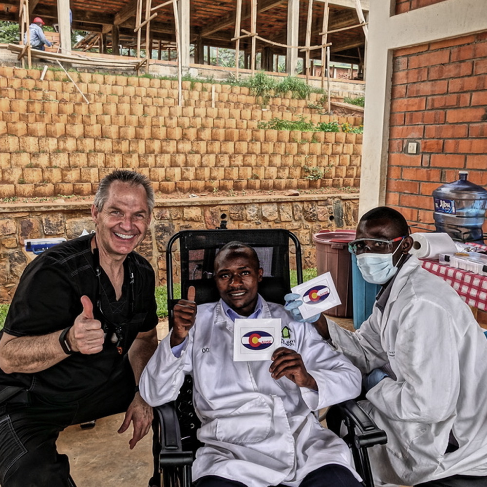 A group of people posing in front of a building, with one person holding up a sign and another wearing a medical coat.