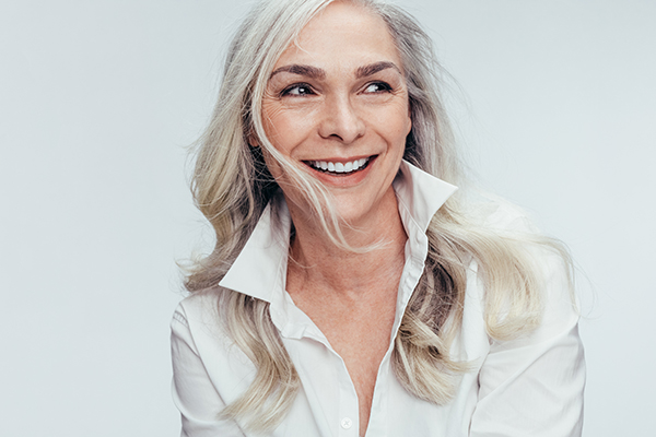 The image is a portrait of a woman with short hair, wearing a white shirt and smiling at the camera.